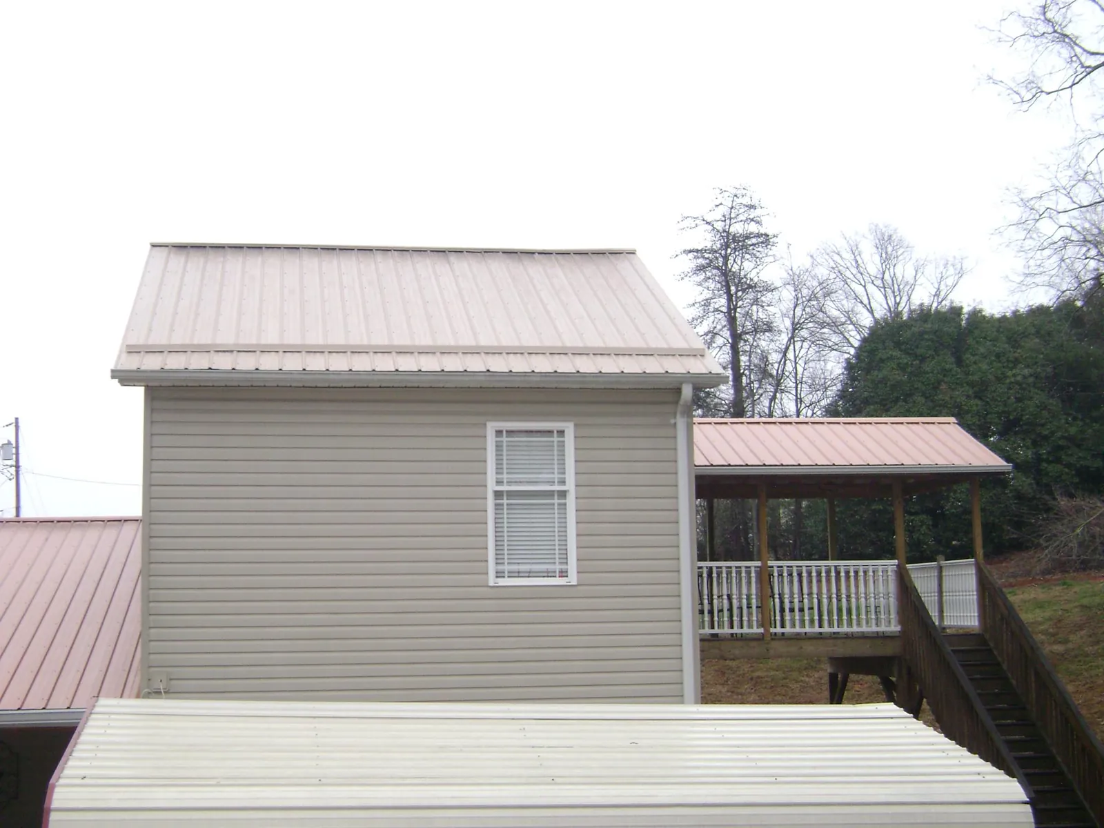 Tan metal roofs on a two story addition and attached porch, from a Roof Replacement job in Bryant